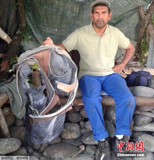 圖為當地時間7月30日，留尼旺島上的一名海岸清潔人員展示他找到的一個手提箱的殘骸。